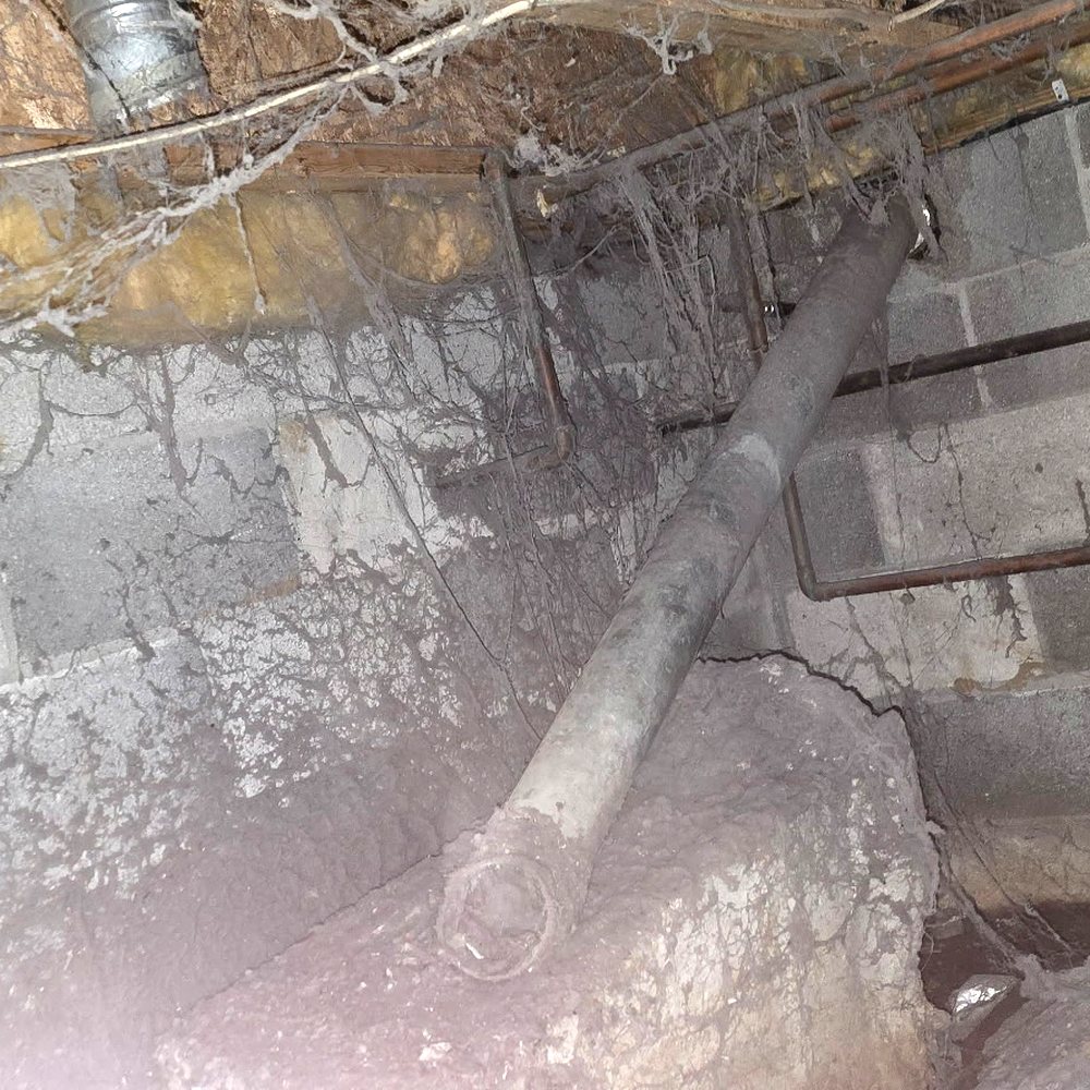 An old unsupported dryer duct in a crawlspace, covered in dust and cobwebs